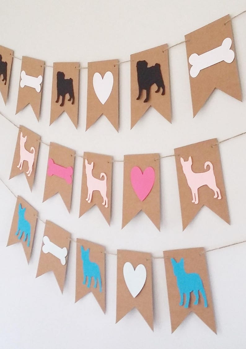 May include: A brown paper banner with cutouts of dogs, hearts, and bones. The dogs are in black, pink, and blue silhouettes. The hearts are white and pink. The bones are white.