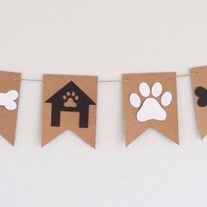 May include: A brown paper banner with black and white paw prints, bones, and dog houses. The banner is strung together with white twine.