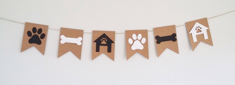 May include: A brown paper banner with black and white paw prints, bones, and dog houses. The banner is strung together with white twine.
