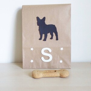 May include: A brown paper gift bag with a black silhouette of a French bulldog, the letter "S" and white stars. A brown dog bone is in the foreground.