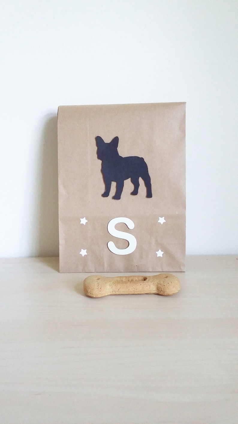 May include: A brown paper gift bag with a black silhouette of a French bulldog, the letter "S" and white stars. A brown dog bone is in the foreground.