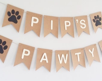 May include: Brown paper banner with white letters spelling "Pip's Pawty" and black paw prints.