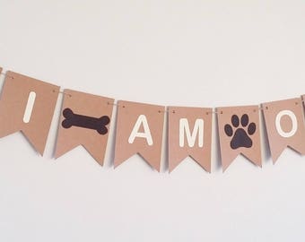 May include: Brown paper banner with the words "I AM ONE" in white letters. The banner also has black paw prints and bone shapes.