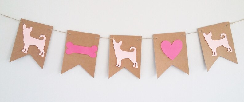 May include: A pink and brown banner with a dog, bone, heart, and dog silhouette. The banner is made of brown paper and has a string running through it.