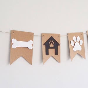 May include: A brown paper banner with black and white paw prints, a bone, a dog house, and the word "home" in white. The banner is strung with twine.
