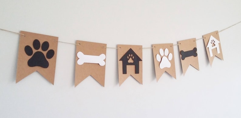 May include: A brown paper banner with black and white paw prints, a bone, a dog house, and the word "home" in white. The banner is strung with twine.