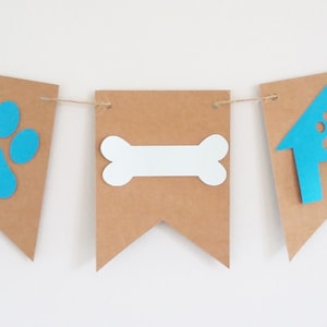 May include: A brown paper banner with blue and white cutouts. The banner has three sections with a paw print, a bone, and a doghouse.