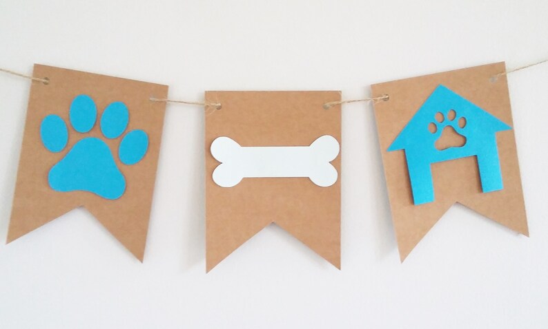 May include: A brown paper banner with blue and white cutouts. The banner has three sections with a paw print, a bone, and a doghouse.