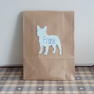 May include: A brown paper bag with a white silhouette of a French bulldog with the name "Frank" written on it.