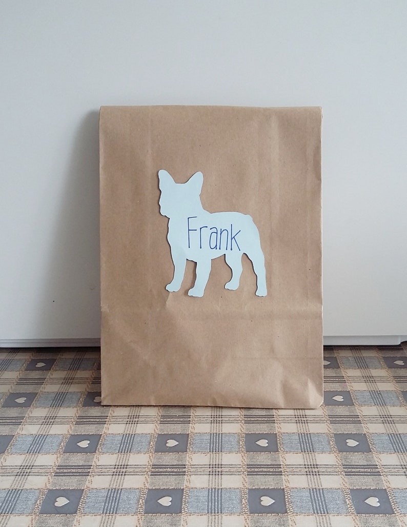 May include: A brown paper bag with a white silhouette of a French bulldog with the name "Frank" written on it.
