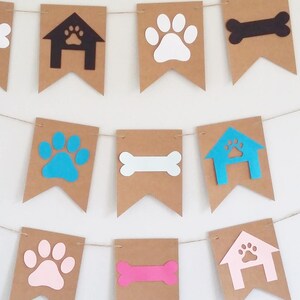May include: A brown paper banner with dog-themed cutouts. The banner features paw prints in white, pink, blue, and turquoise, bone shapes in black, white, and pink, and dog house shapes in black, blue, and pink.