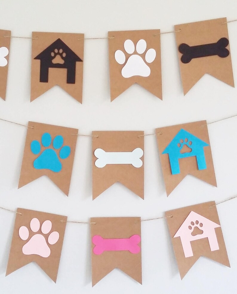 May include: A brown paper banner with dog-themed cutouts. The banner features paw prints in white, pink, blue, and turquoise, bone shapes in black, white, and pink, and dog house shapes in black, blue, and pink.