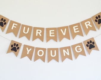 May include: A brown paper banner with white letters spelling "FOREVER YOUNG" and black paw prints. The banner is strung on a white string.