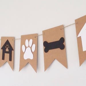 May include: Brown paper banner with white and black dog-themed cutouts. The banner includes paw prints, a bone, a doghouse, and a paw print inside a doghouse.