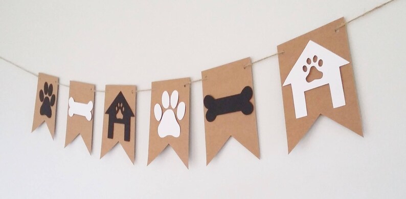 May include: Brown paper banner with white and black dog-themed cutouts. The banner includes paw prints, a bone, a doghouse, and a paw print inside a doghouse.
