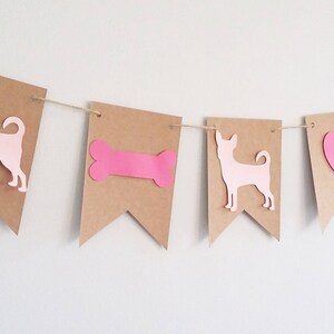 May include: A brown paper banner with pink cutouts of a dog, a bone, a heart, and a dog. The banner is strung with twine.