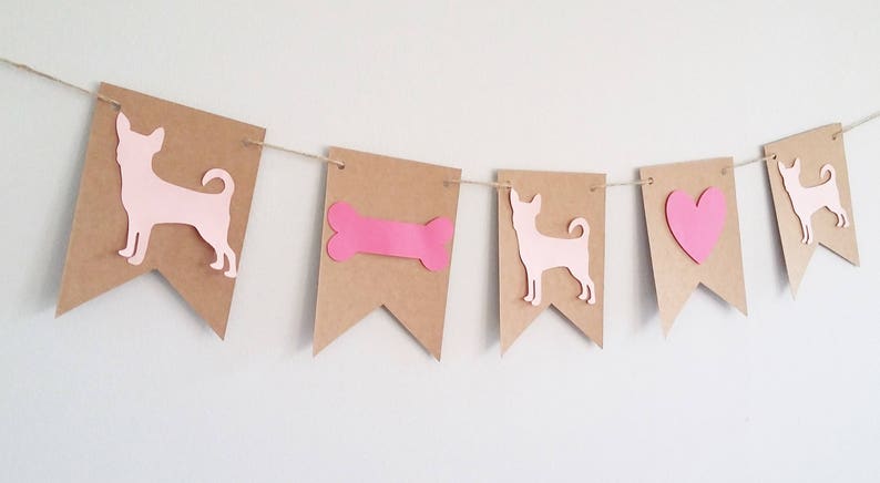 May include: A brown paper banner with pink cutouts of a dog, a bone, a heart, and a dog. The banner is strung with twine.