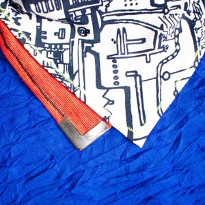 Pode incluir: Um tecido azul com uma guarni&ccedil;&atilde;o vermelha e preta. A guarni&ccedil;&atilde;o tem uma pe&ccedil;a de metal prateada na extremidade. O tecido tem um padr&atilde;o texturizado.