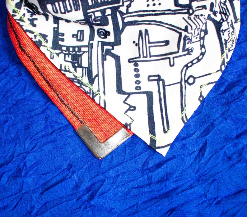 Pode incluir: Um tecido azul com uma guarni&ccedil;&atilde;o vermelha e preta. A guarni&ccedil;&atilde;o tem uma pe&ccedil;a de metal prateada na extremidade. O tecido tem um padr&atilde;o texturizado.