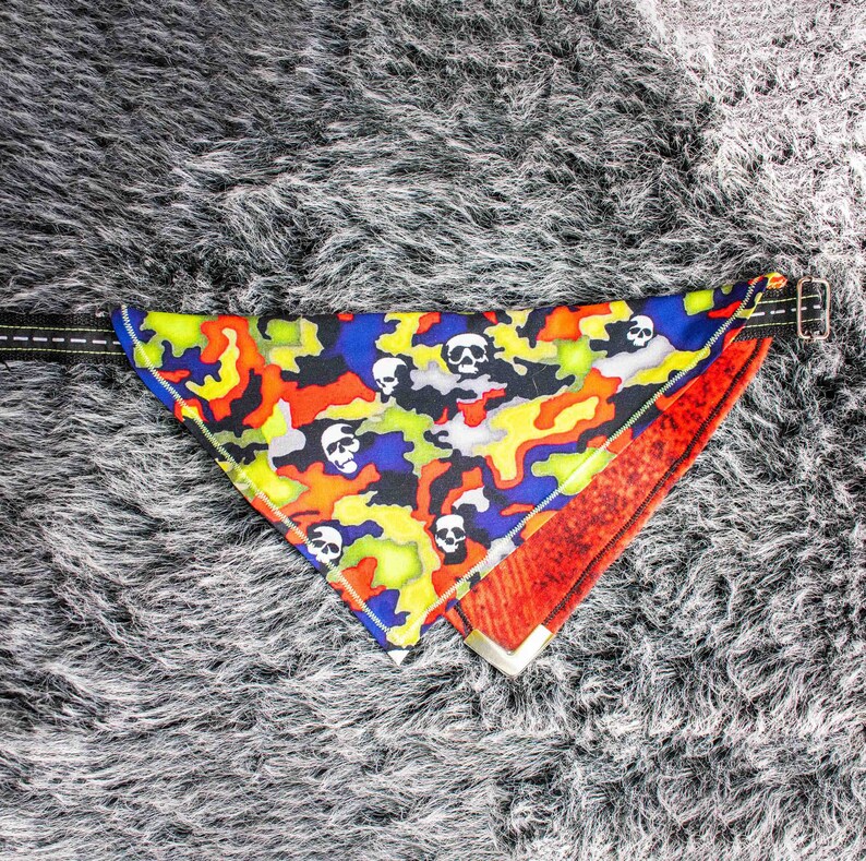 Pode incluir: Um bandana colorido com um padr&atilde;o de camuflagem e desenhos de caveiras. O bandana &eacute; vermelho, amarelo, azul e preto com caveiras brancas. O bandana tem uma fivela dourada.
