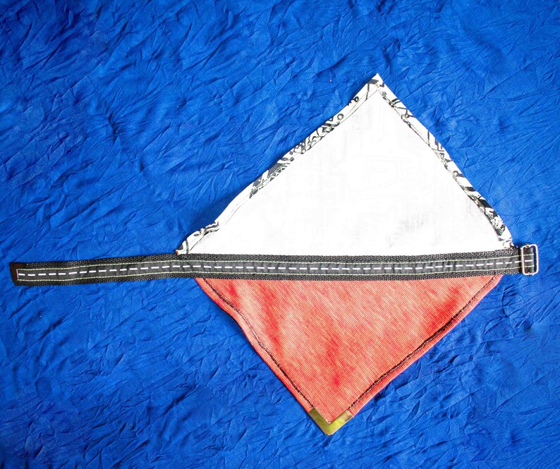 Pode incluir: Um bandana vermelho e branco com uma al&ccedil;a preta. O bandana &eacute; dobrado em forma de tri&acirc;ngulo e tem um forro de tecido branco.