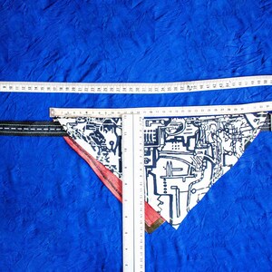 Pode incluir: Um bandana branco e preto com padr&atilde;o e borda vermelha, medido com uma r&eacute;gua. O bandana est&aacute; sobre uma superf&iacute;cie azul.