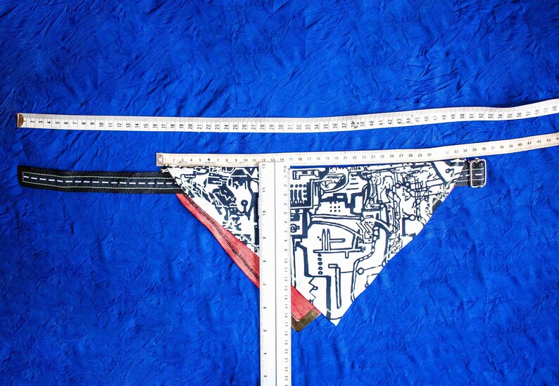 Pode incluir: Um bandana branco e preto com padr&atilde;o e borda vermelha, medido com uma r&eacute;gua. O bandana est&aacute; sobre uma superf&iacute;cie azul.