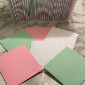 May include: A stack of blank cards in a clear plastic storage container. The cards are in three colors: green, pink, and white. The cards are arranged in a neat stack.