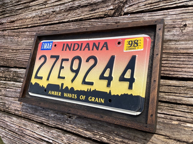 May include: A framed Indiana license plate with the number 27E9244. The plate has a sunset gradient background with the text "Amber Waves of Grain".