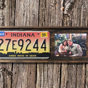 May include: A wooden frame with a vintage Indiana license plate with the number 27E9244 and the text "Amber Waves of Grain". A photo of a couple is in the frame to the right of the license plate.
