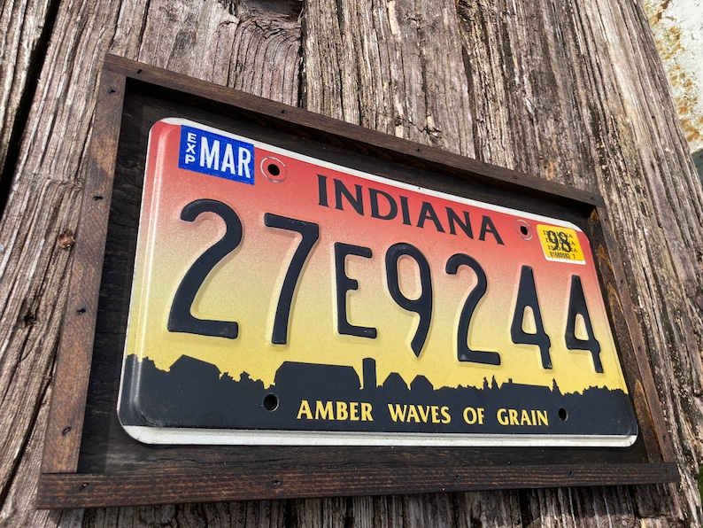 May include: A framed Indiana license plate with the number 27E9244 and the text "Amber Waves of Grain". The plate is red, yellow, and black with a white sticker that says "98".