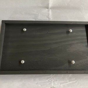 May include: A black wooden frame with four silver screws attached to the surface.