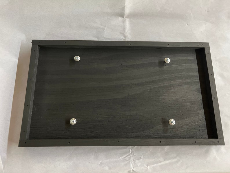 May include: A black wooden frame with four silver screws attached to the surface.