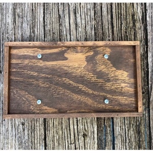 May include: A rectangular wooden sign with a dark brown stain. The sign has four screws holding it together. The sign is on a wooden background.