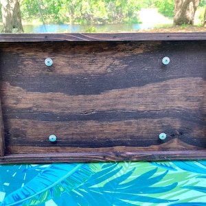 May include: The back of a wooden box with four silver screws securing the lid. The box is dark brown with a wood grain pattern.