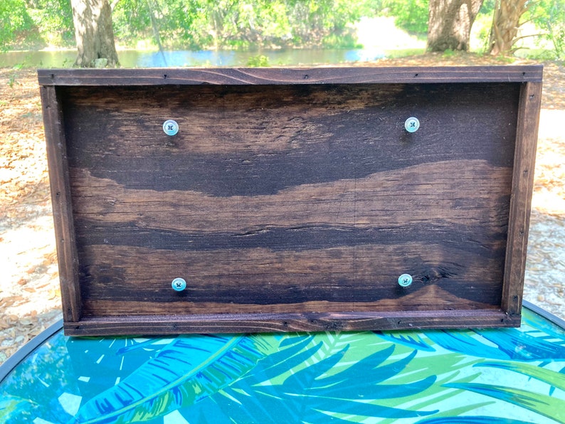 May include: The back of a wooden box with four silver screws securing the lid. The box is dark brown with a wood grain pattern.