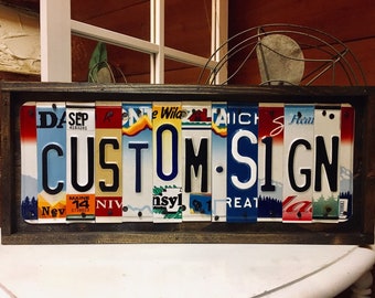 May include: A framed sign spelling "CUSTOM SIGN" using vintage license plates from different states. The sign is made of wood and has a rustic look.