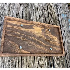 May include: A rectangular wooden sign with a dark brown stain. The sign has a raised frame and four silver screws securing it to the surface.