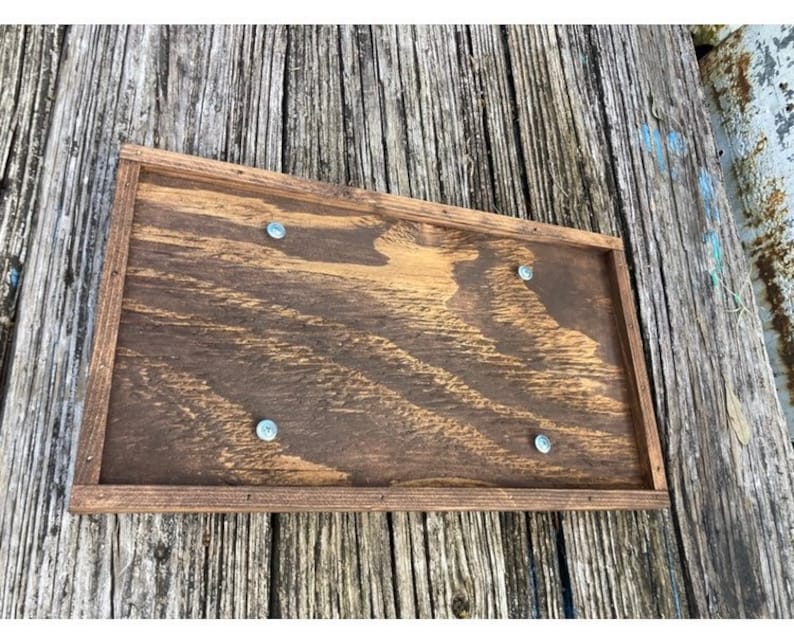 May include: A rectangular wooden sign with a dark brown stain. The sign has a raised frame and four silver screws securing it to the surface.
