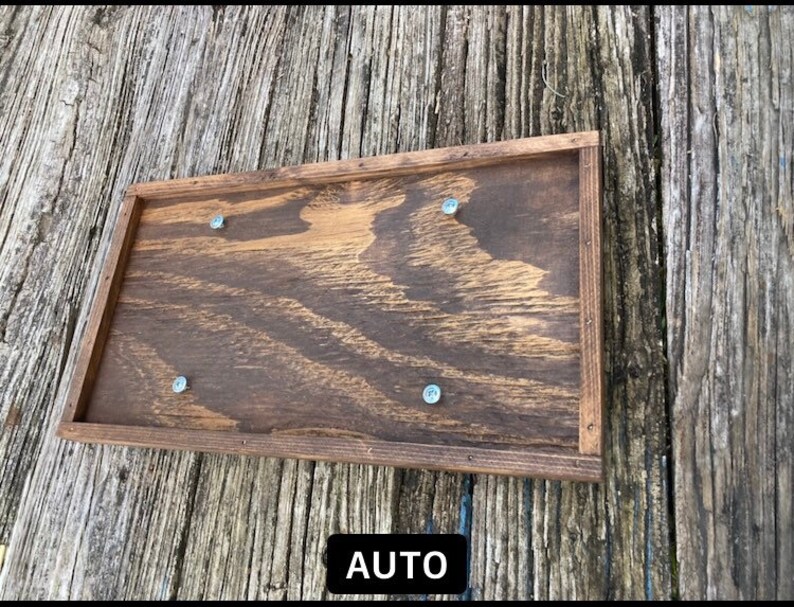 May include: A wooden sign with a dark brown stain and a natural wood frame. The sign has four silver screws holding it together. The sign says "AUTO" in white letters.