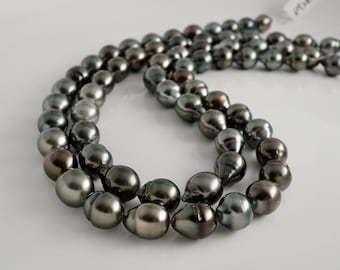 May include: A strand of dark gray Tahitian pearls. The pearls are round and have a slight iridescent sheen.