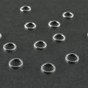 Peut inclure: Un ensemble de 13 anneaux de saut argentés, disposés en forme de diamant sur une surface gris foncé.