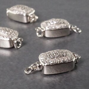 May include: Four silver-toned, rectangular clasps with clear crystal embellishments. Each clasp has a small loop on either side.