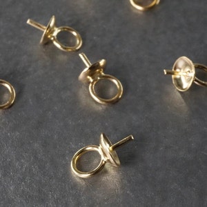 May include: Five gold-toned metal bead tips with a loop on one end and a small hole on the other end. The bead tips are arranged on a gray surface.