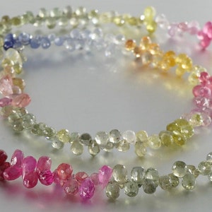 May include: A strand of faceted gemstone beads in a rainbow of colors, including pink, red, yellow, green, blue, and purple. The beads are strung on a clear thread and are arranged in a loose, flowing pattern.