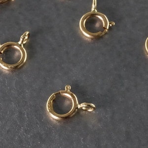 May include: Five gold-toned metal clasps for jewellery making. Each clasp has a round ring and a spring-loaded closure.