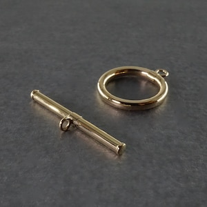 Könnte beinhalten: Goldfarbener Metall-Schiebeverschluss mit einem runden Ring und einer geraden Stange. Der Verschluss wird für die Schmuckherstellung verwendet.
