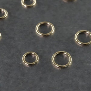 以下が含まれることがあります： グレーの表面に、さまざまなサイズのゴールドのジャンプリングが8個並んでいます。