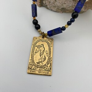Colar com pingente de carta de tarô, joia com tom dourado e pedras preciosas, o mundo, carta de tarô, lápis-lazúli