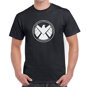 May include: Black t-shirt with a white logo of the Strategic Homeland Intervention Enforcement Logistics Division, also known as S.H.I.E.L.D., featuring a white eagle with wings spread and a circle around it.